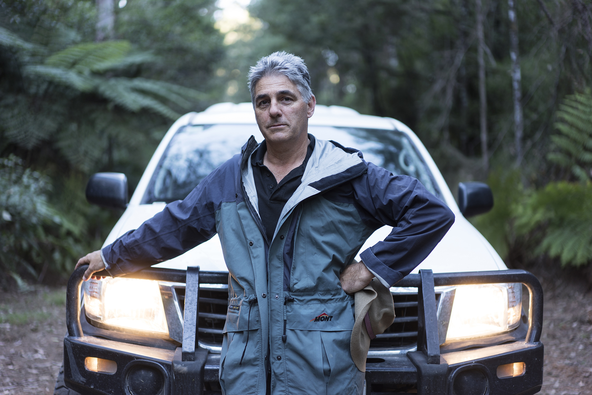 Professor David Lindenmayer in a forest standing in front of a vehicle.